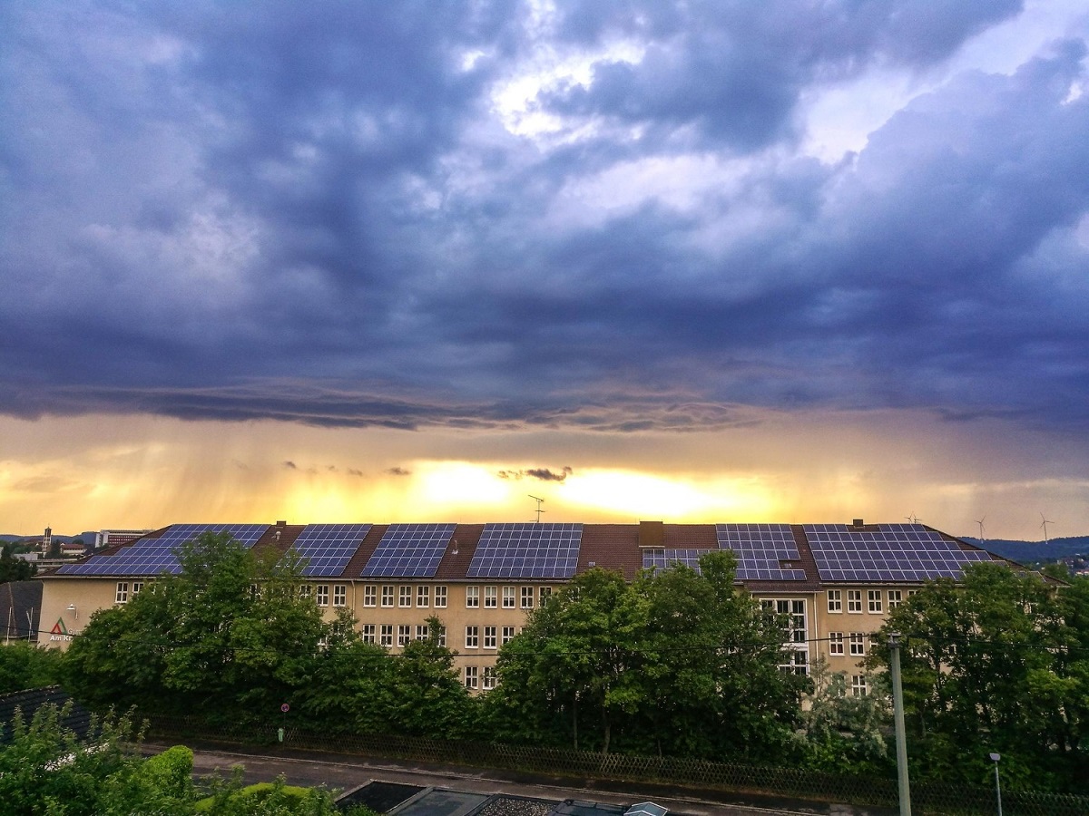 Solar panels on a building during cloudy weather, with a dramatic, stormy sky and a bright sunset on the horizon.